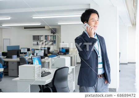 一個年輕的商人,通過在清晨獨自一人去辦公室與智能手機交談 一個年輕的商人,通過在清晨獨自一人去辦公室與智能手機交談 68689472