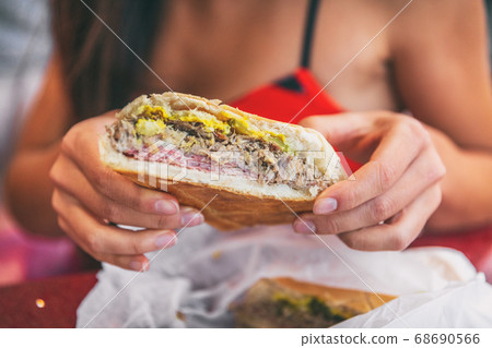 Cuban sandwich closeup woman holding local food at typical cafe outside. Pressed cuban bread with roasted pork, salami sausage, swiss cheese, mustard, typical cuba dish Cuban sandwich closeup woman holding local food at typical cafe outside. Pressed cuban bread with roasted pork, salami sausage, swiss cheese, mustard, typical cuba dish 68690566