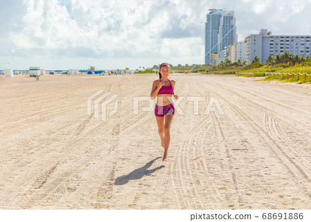Fit woman training outdoors running barefoot on Miami south beach run jogging workout female Asian athlete. Happy healthy fitness person cardio jog in sun summer lifestyle 68691886