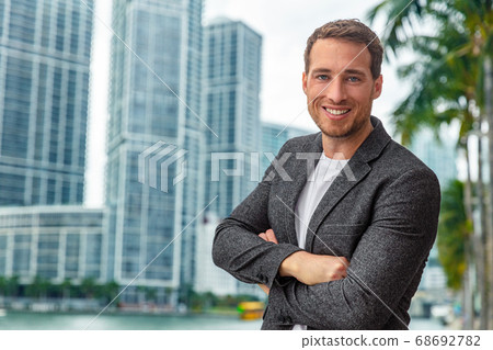 Happy smiling young caucasian businessman man confident with crossed arms portrait wearing smart casual professional blazer on urban city background cityscape Happy smiling young caucasian businessman man confident with crossed arms portrait wearing smart casual professional blazer on urban city background cityscape 68692782