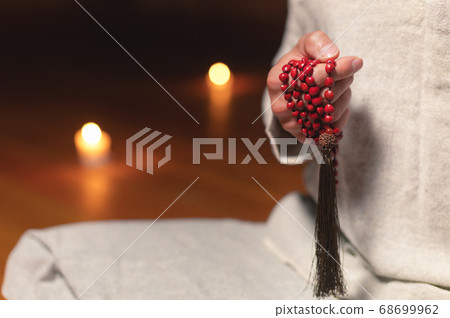 A close-up of the monk's hands hold red rosaries against the background of the wooden floor of the practice room and lit candles A close-up of the monk's hands hold red rosaries against the background of the wooden floor of the practice room and lit candles 68699962