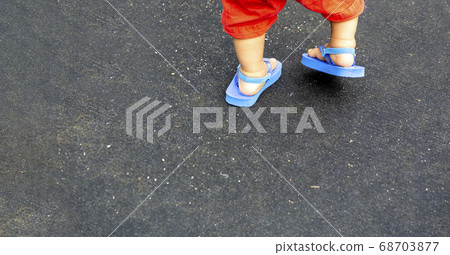 Foot of child walking and blue beach sandals and black back and copy space 68703877
