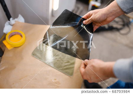 Male worker holds sheet of car tinting 68703984
