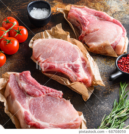 Tree bunch raw pork chops arranged with herbs, oil and spices. Cooking meat. On dark background Square. Tree bunch raw pork chops arranged with herbs, oil and spices. Cooking meat. On dark background Square. 68708050