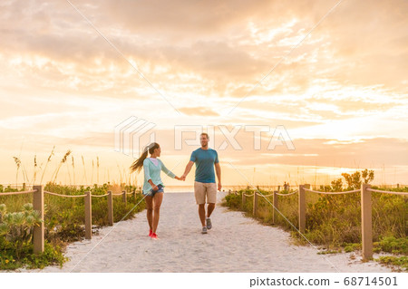 Happy young couple in love walking on romantic beach stroll at sunset. Lovers holding hands on Florida vacation holidays. People walking on summer evening lifestyle 68714501