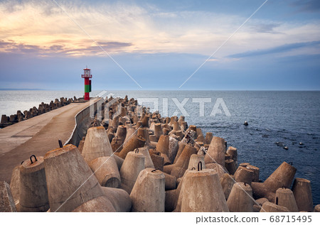 Pier with lighthouse protected by concrete breakwater tetrapods at sunset. Pier with lighthouse protected by concrete breakwater tetrapods at sunset. 68715495