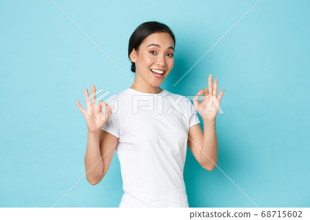 Pretty confident asian smiling girl ensure everything OK, under control. Woman encourage all good, showing okay gesture and nod in approval, guarantee quality, standing satisfied blue background 68715602