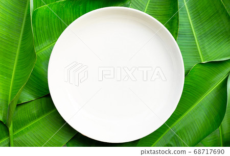 Empty white ceramic plate on banana leaves Empty white ceramic plate on banana leaves 68717690