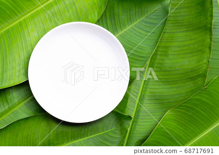 Empty white ceramic plate on banana leaves Empty white ceramic plate on banana leaves 68717691