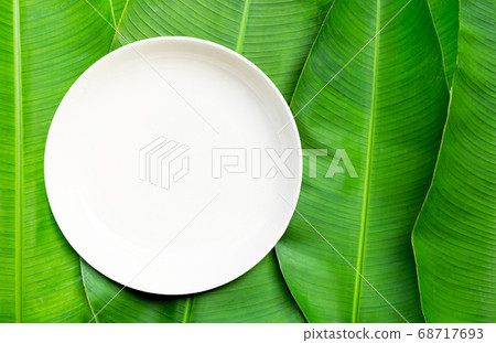 Empty white ceramic plate on banana leaves Empty white ceramic plate on banana leaves 68717693