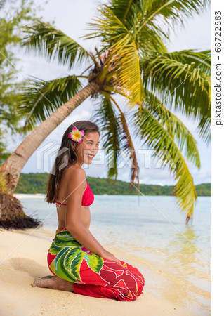Beach woman relaxing on Bora Bora Tahiti island under the sun wearing polynesian skirt and monoi flower with palm tree background. Polynesia culture travel concept 68722883