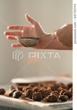young female hands sprinkle fresh chocolate truffles with cocoa powder on concrete countertop young female hands sprinkle fresh chocolate truffles with cocoa powder on concrete countertop 68730743