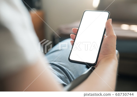 Young woman sitting in chair and holding smartphone with white screen Young woman sitting in chair and holding smartphone with white screen 68730744