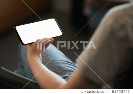 Young woman hold smarphone with white screen while sitting in a chair 68730745