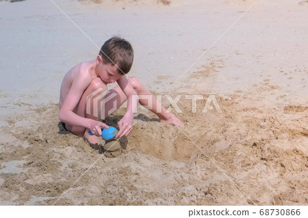 Child boy playing on sand beach digging shovel and trying to build sand tower. 68730866