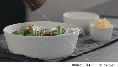 man seasoning salad with kumato tomatoes and spinach in white bowl 68730988
