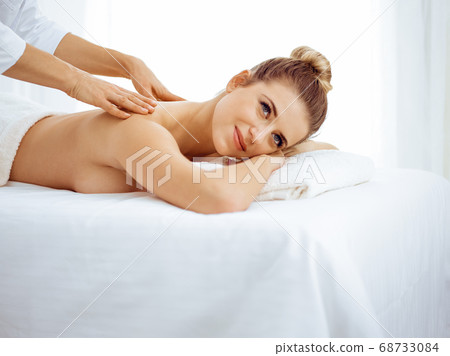 Young and blonde woman enjoying massage of back in spa salon. Beauty concept Young and blonde woman enjoying massage of back in spa salon. Beauty concept 68733084