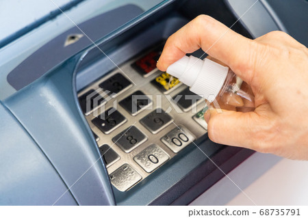 Person spraying sanitizer disinfectant onto ATM Person spraying sanitizer disinfectant onto ATM 68735791