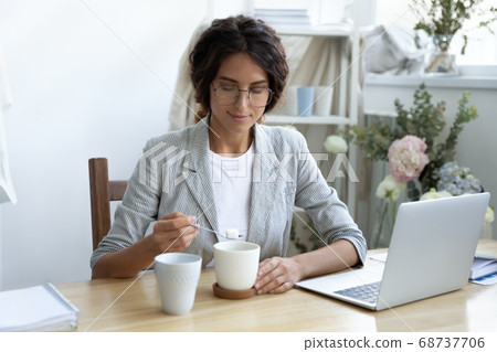Happy young businesswoman adding refined sugar to cup of coffee. 68737706