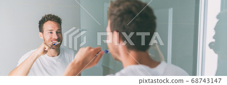 Brushing teeth man getting ready in the morning banner panorama. Guy looking in mirror of home bathroom using toothbrush in hygiene routine for clean dental oral care banner panorama Brushing teeth man getting ready in the morning banner panorama. Guy looking in mirror of home bathroom using toothbrush in hygiene routine for clean dental oral care banner panorama 68743147