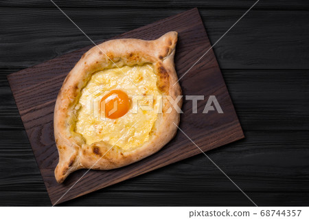Adjarian Khachapuri on a brown board on a black Adjarian Khachapuri on a brown board on a black 68744357