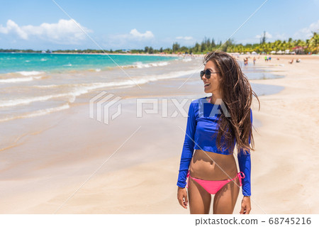 Puerto Rico beach vacation woman relaxing in San Juan wearing rash guard solar protection surf clothing and bikini happy on summer holidays travel destination. Puerto Rico beach vacation woman relaxing in San Juan wearing rash guard solar protection surf clothing and bikini happy on summer holidays travel destination. 68745216