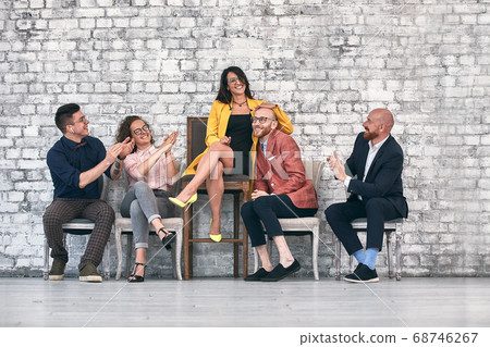 Beautiful cheerful professional woman wearing eyeglasses seated with male co-workers and team leader at work Beautiful cheerful professional woman wearing eyeglasses seated with male co-workers and team leader at work 68746267