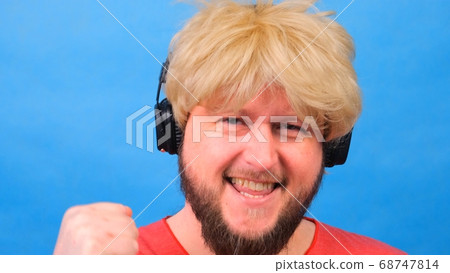freaky fat man in a wig and a pink T-shirt in his hands listens to music on headphones and dances on 68747814