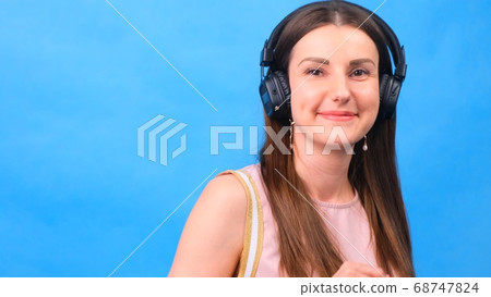 Energy girl with headphones listening to music on a blue background, close up Energy girl with headphones listening to music on a blue background, close up 68747824