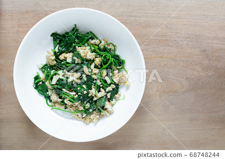 top view of stir fried ivy gourd with egg in a ceramic dish on wooden table. top view of stir fried ivy gourd with egg in a ceramic dish on wooden table. 68748244