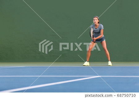 Tennis player woman standing ready to play waiting to receive serve. Outdoor fitness instructor focused playing on hard court on green background Tennis player woman standing ready to play waiting to receive serve. Outdoor fitness instructor focused playing on hard court on green background 68750710
