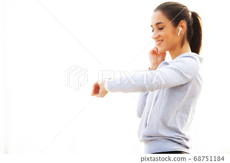 Photo of Joyful Fitness Woman 30s in Sportswear Touching Bluetooth Earpod and Holding Mobile Phone, While Resting in Green Park 68751184