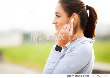Photo of Joyful Fitness Woman 30s in Sportswear Touching Bluetooth Earpod and Holding Mobile Phone, While Resting in Green Park 68751185