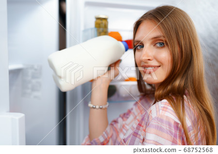 Portrait of a young blonde woman taking food from her fridge Portrait of a young blonde woman taking food from her fridge 68752568