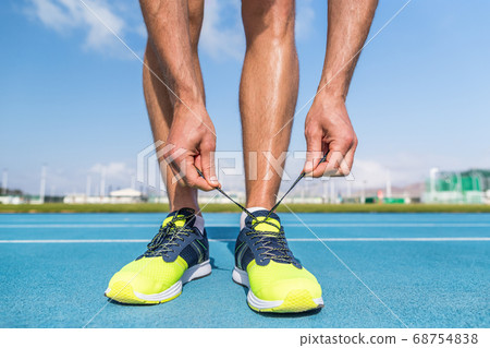 Runner tying running shoes laces on run tracks lanes in stadium getting ready for race competition outdoor on track and field. Sport athlete man jogging motivation 68754838
