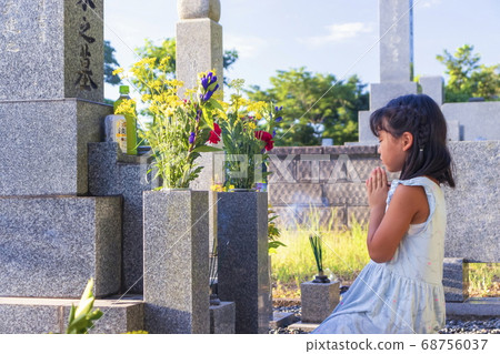 A visit to the grave A girl silently puts her hands together in front of the grave 68756037