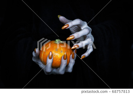 Small pumpkin in witches knotty hand. Scary undead pale fingers with long sharp claws in the dark, low key, selected focus. 68757813
