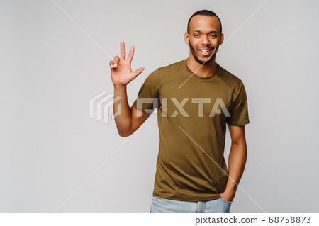 Joyful friendly african-american young man in green t-shirt pointing or showing THREE by finger 68758873