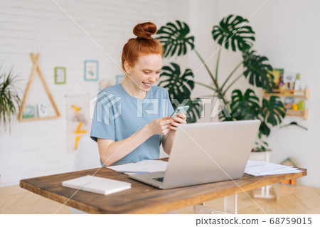 Cheerful happy redhead young woman browsing internet on phone at workplace. 68759015