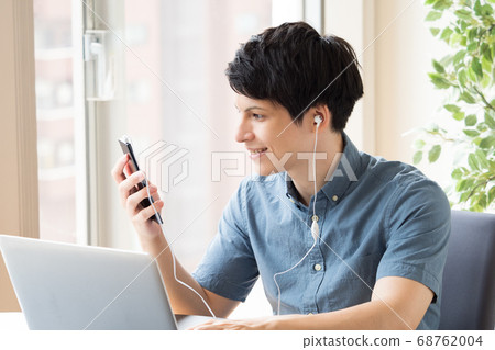 A man who makes earphone calls with a smartphone during work 68762004