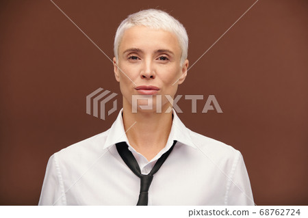 Serious mature blond businesswoman in white shirt and black tie looking at you 68762724