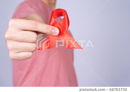 Red AIDS awareness ribbon holding by man on grey Red AIDS awareness ribbon holding by man on grey 68763730