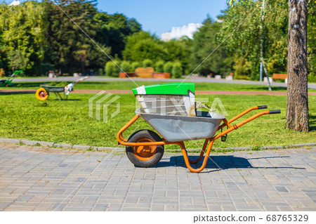 Green metal garden wheelbarrow on the grass in the garden for cleaning the territory 68765329