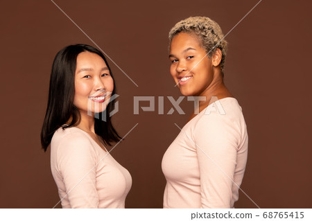 Two young cheerful females with toothy smiles standing opposite one another 68765415