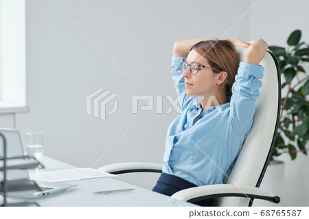 Young restful businesswoman keeping hands behind head while relaxing in armchair 68765587