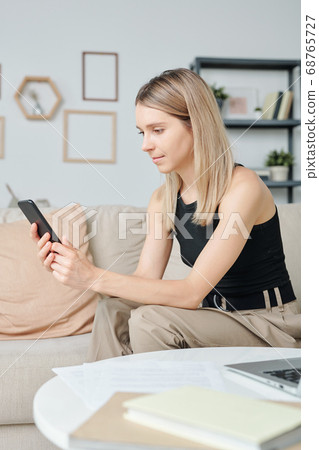 Blond pretty girl in casualwear with smartphone scrolling through contacts 68765727