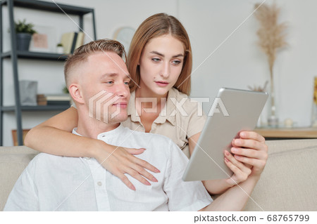 Affectionate woman with tablet showing husband nice clothing in online shop Affectionate woman with tablet showing husband nice clothing in online shop 68765799