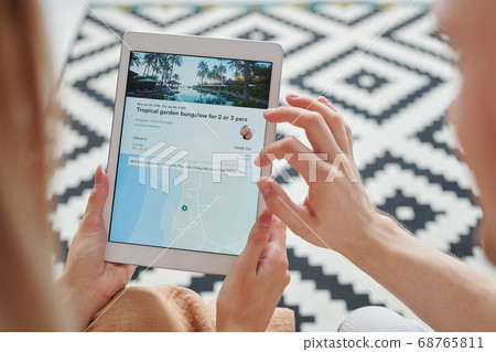 Hands of young man over touchscreen held by his wife scrolling through websites Hands of young man over touchscreen held by his wife scrolling through websites 68765811