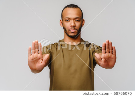 african american young man gesturing STOP with his hand over light grey background african american young man gesturing STOP with his hand over light grey background 68766070