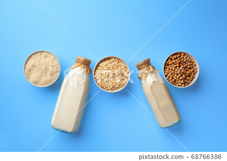 Two glass bottles of non-dairy vegan milk with bowls of grains top view 68766386